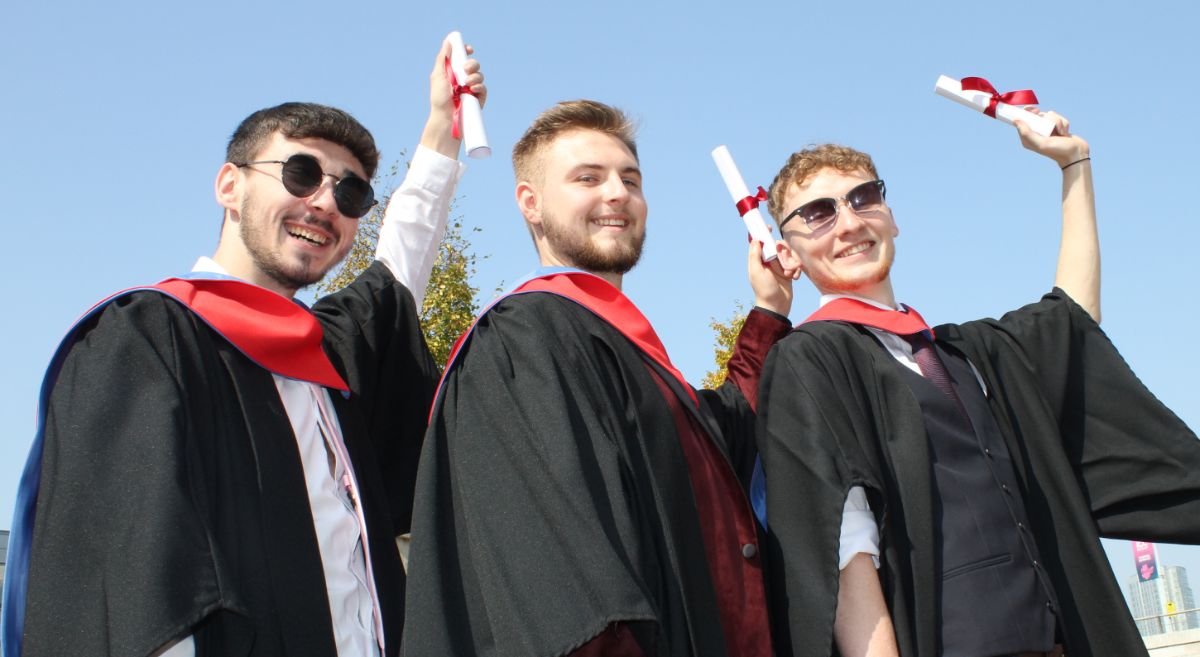 3 male graduates holding scrolls on a sunny day