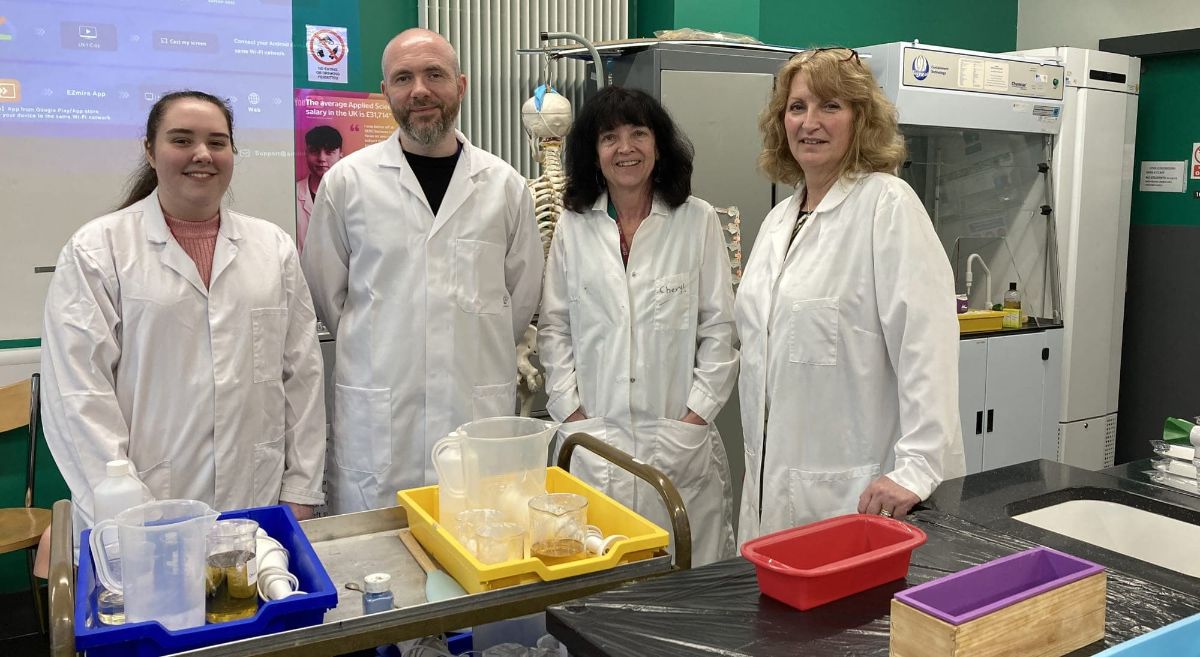 Three females and one male wearing white lab coats, smiling to camera, pictured in lab setting