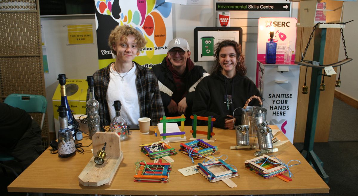 three people sat behind a table selling products