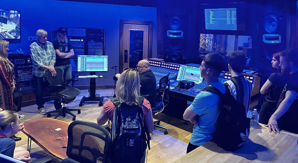 Students pictured in music studio with  monitors and mixing board whilst man gives talk