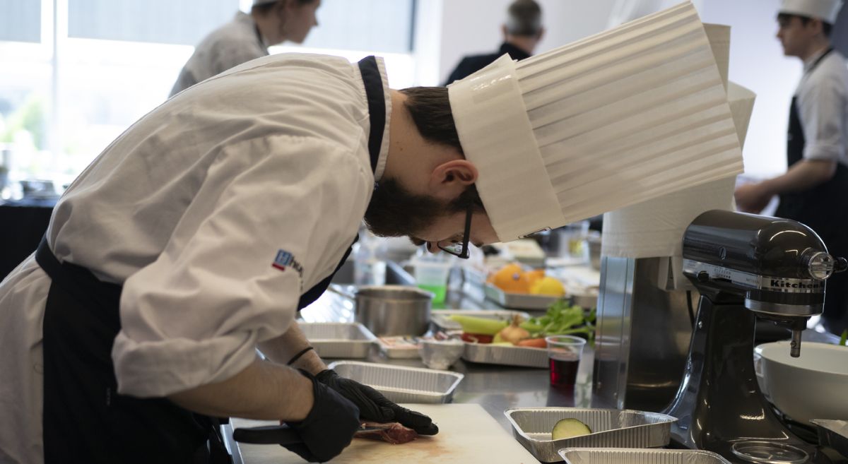 Student Dylan Murphy in chef whites and dark apron prepping food in professional kitchen during competition