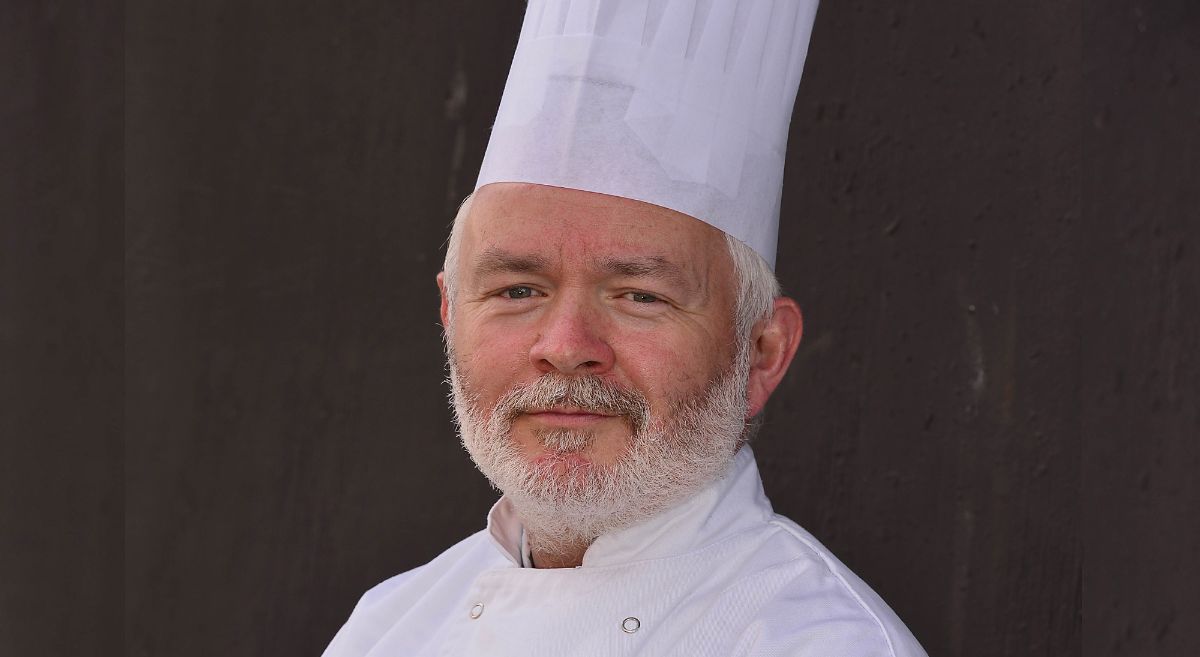 Chef Lecturer Paul Monaghan pictured in chef whites against a dark backround