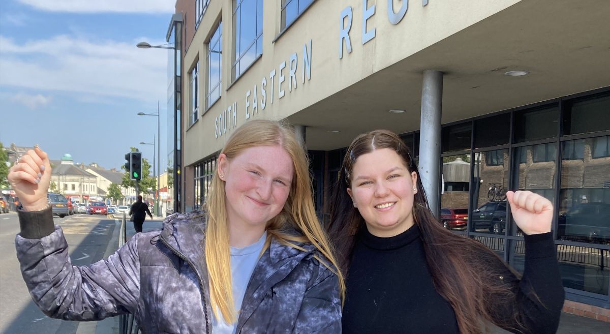 Two females, smiling to camera and punching the air, pictured outside Downpatrick Campus