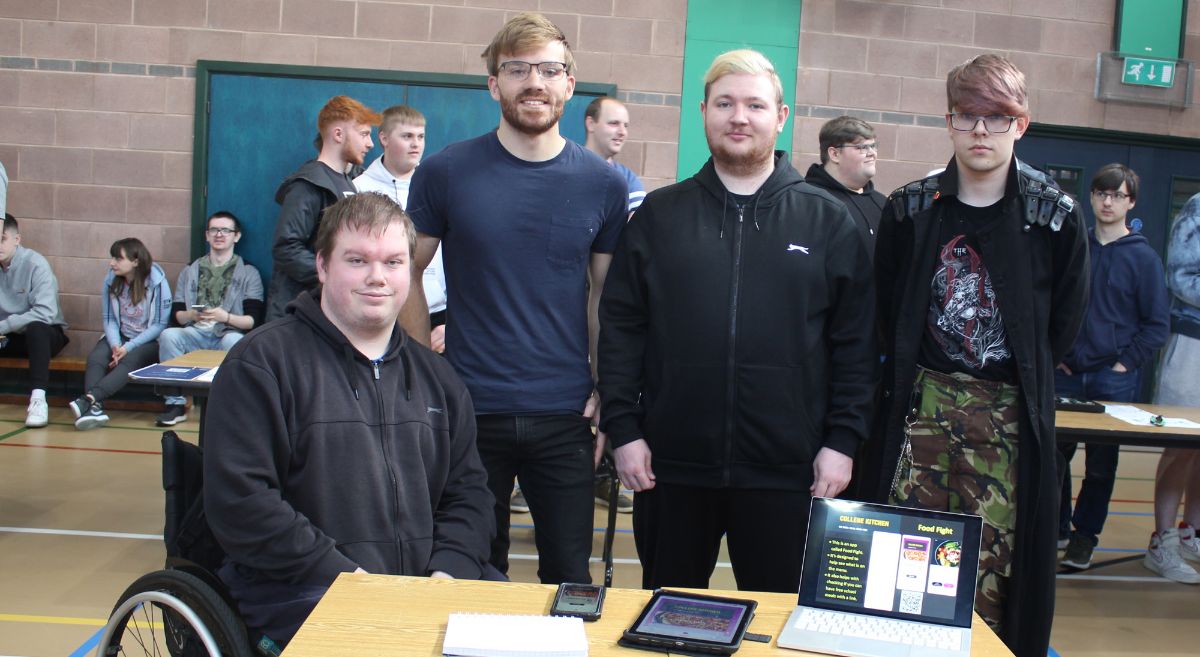 Group of four male students behind table displaying computer and tablet