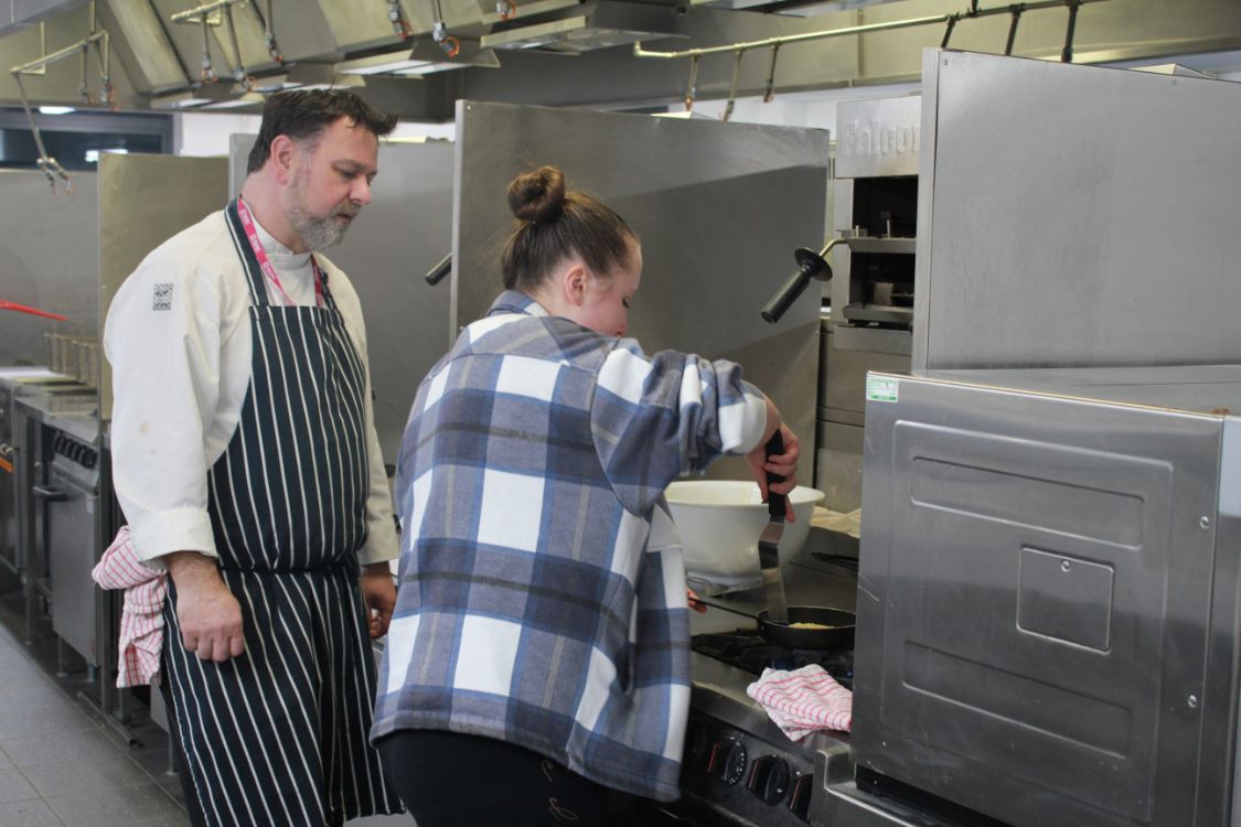 aspiring chef working in a kitchen with lecturer watching