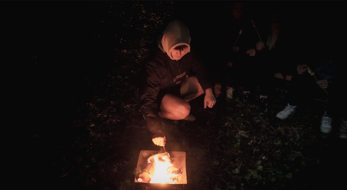 Young male sitting in front of a camp fire.