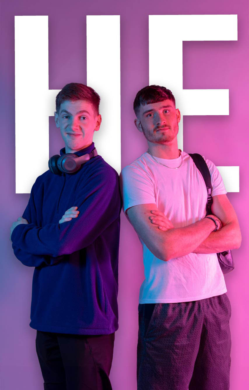 Two male students standing with the letters HE behind them